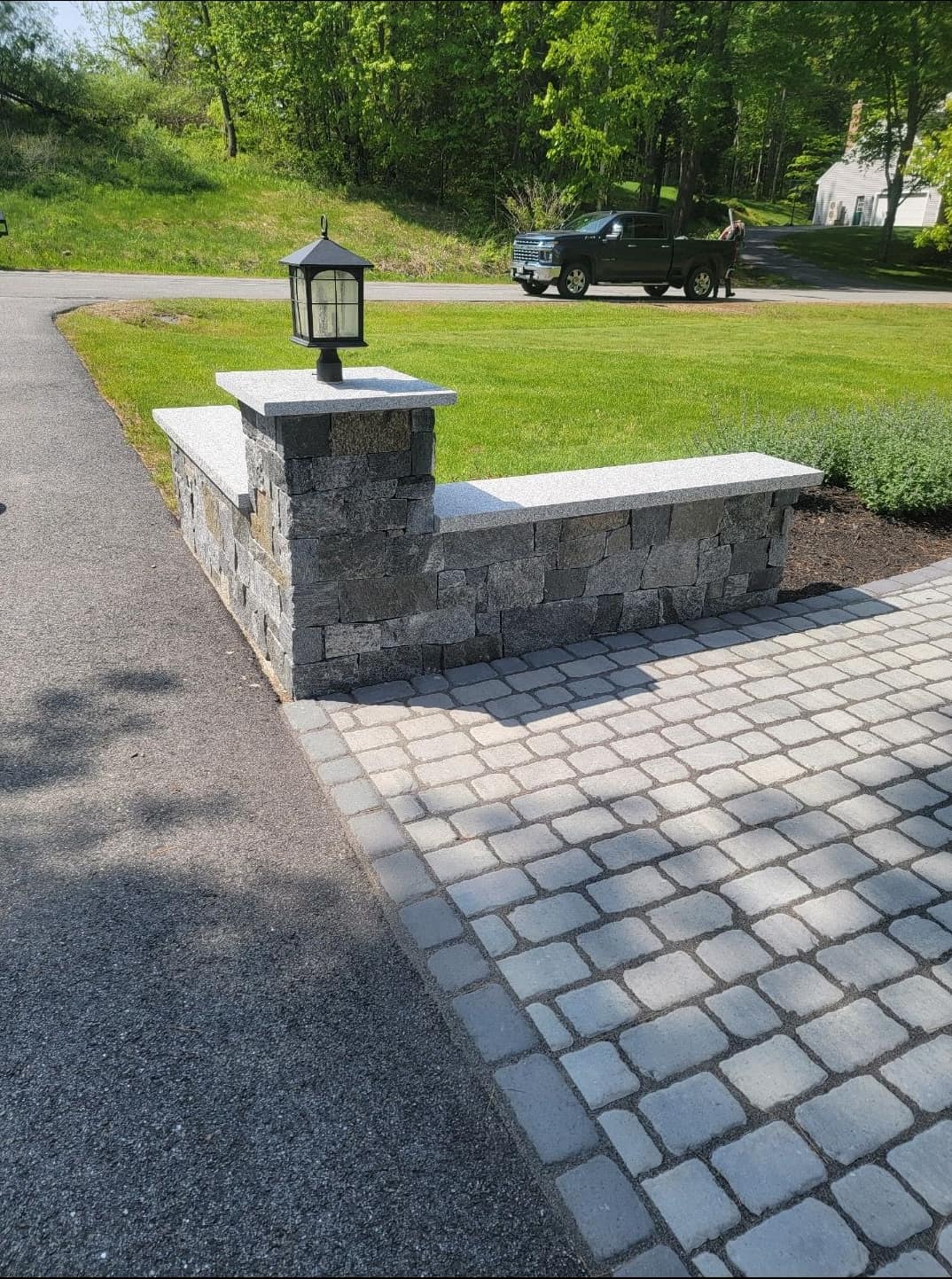 Granite veneer retaining wall with a lantern-topped stone pillar and cobblestone apron
